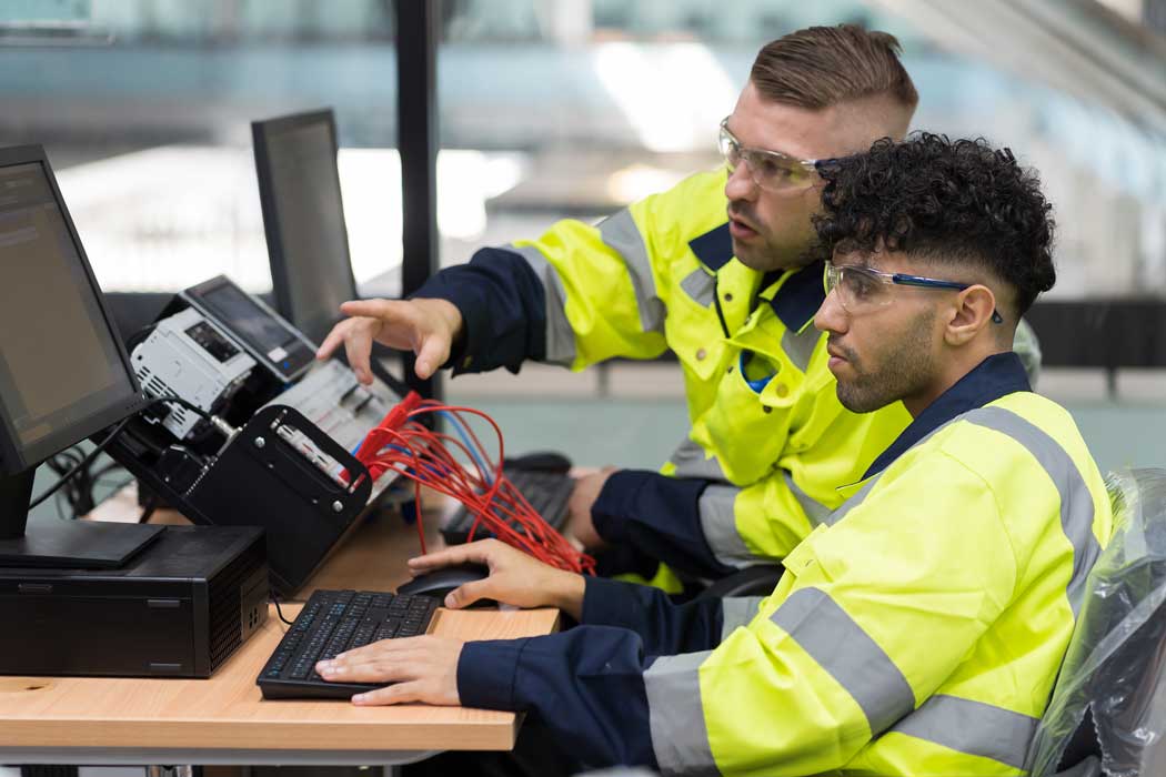 Employer and apprentice sat at a desk in high vis workwear using electrical equipment